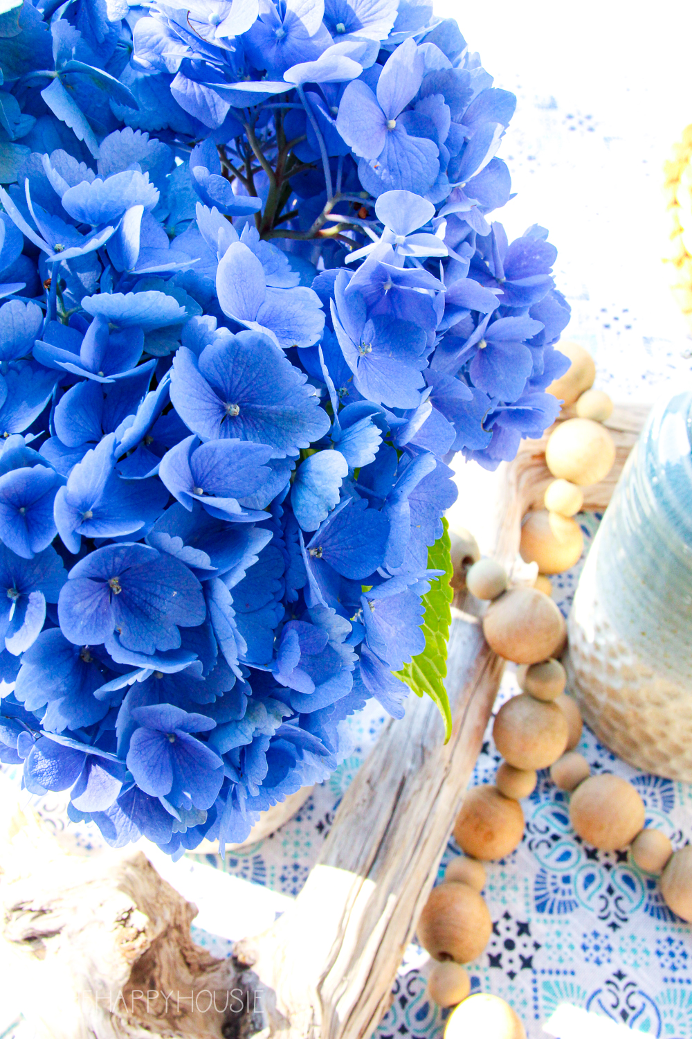 Blue hydrangeas are in a vase next to the driftwood.