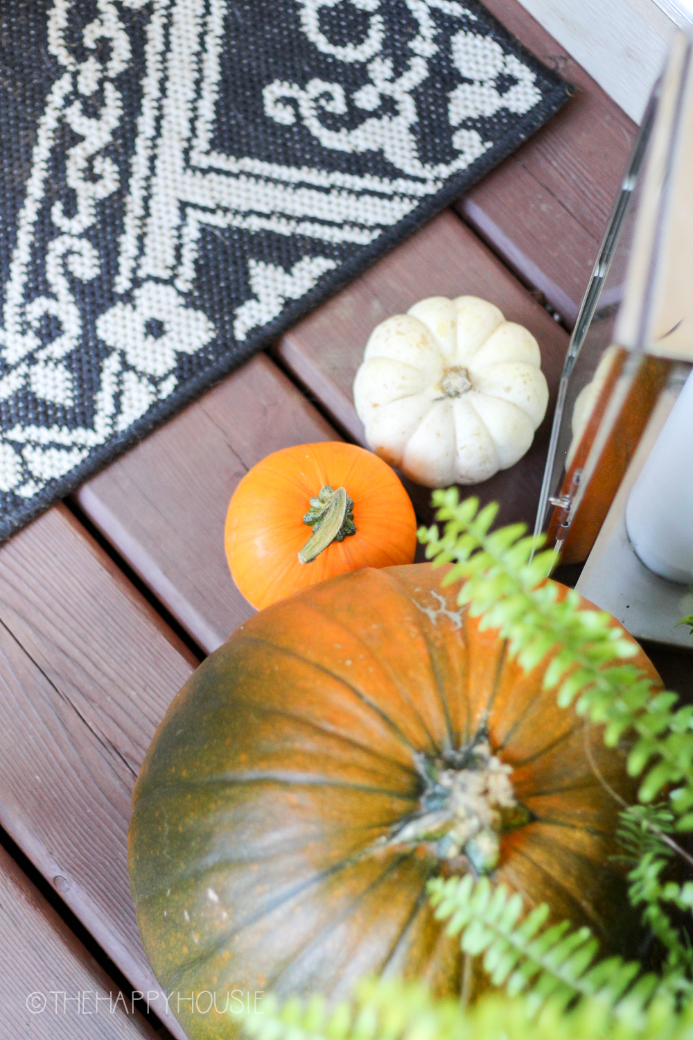 There is a large pumpkins beside the smaller ones on the porch with a black and white mat beside them.