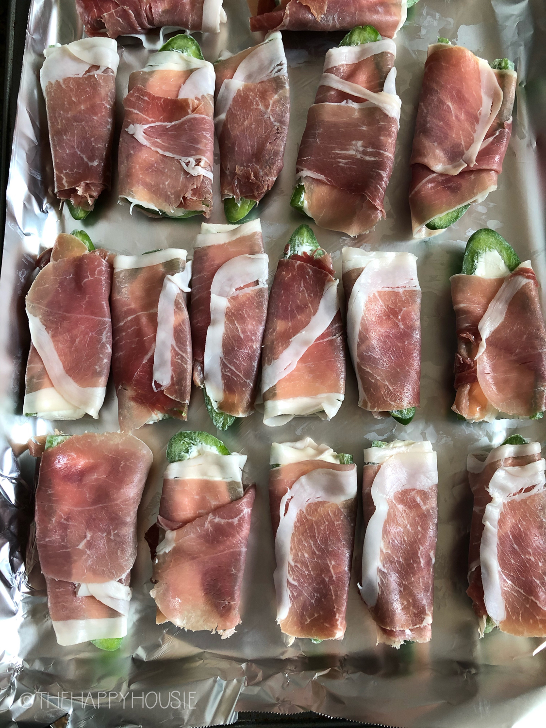 The wrapped jalapeños in prosciutto on a baking tray.