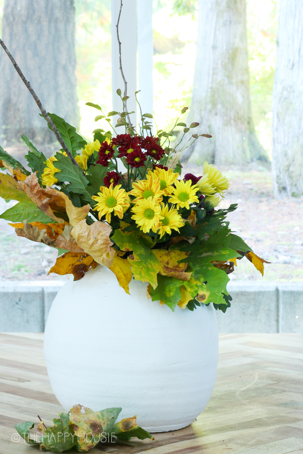 The flowers, leaves and branches in the vase on the counter.