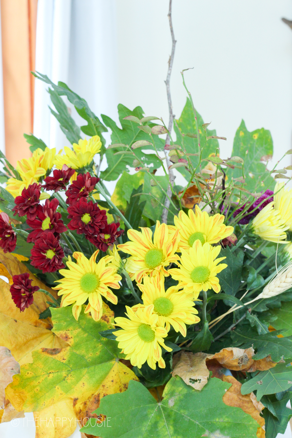 Yellow and red flowers with leaves in a vase.
