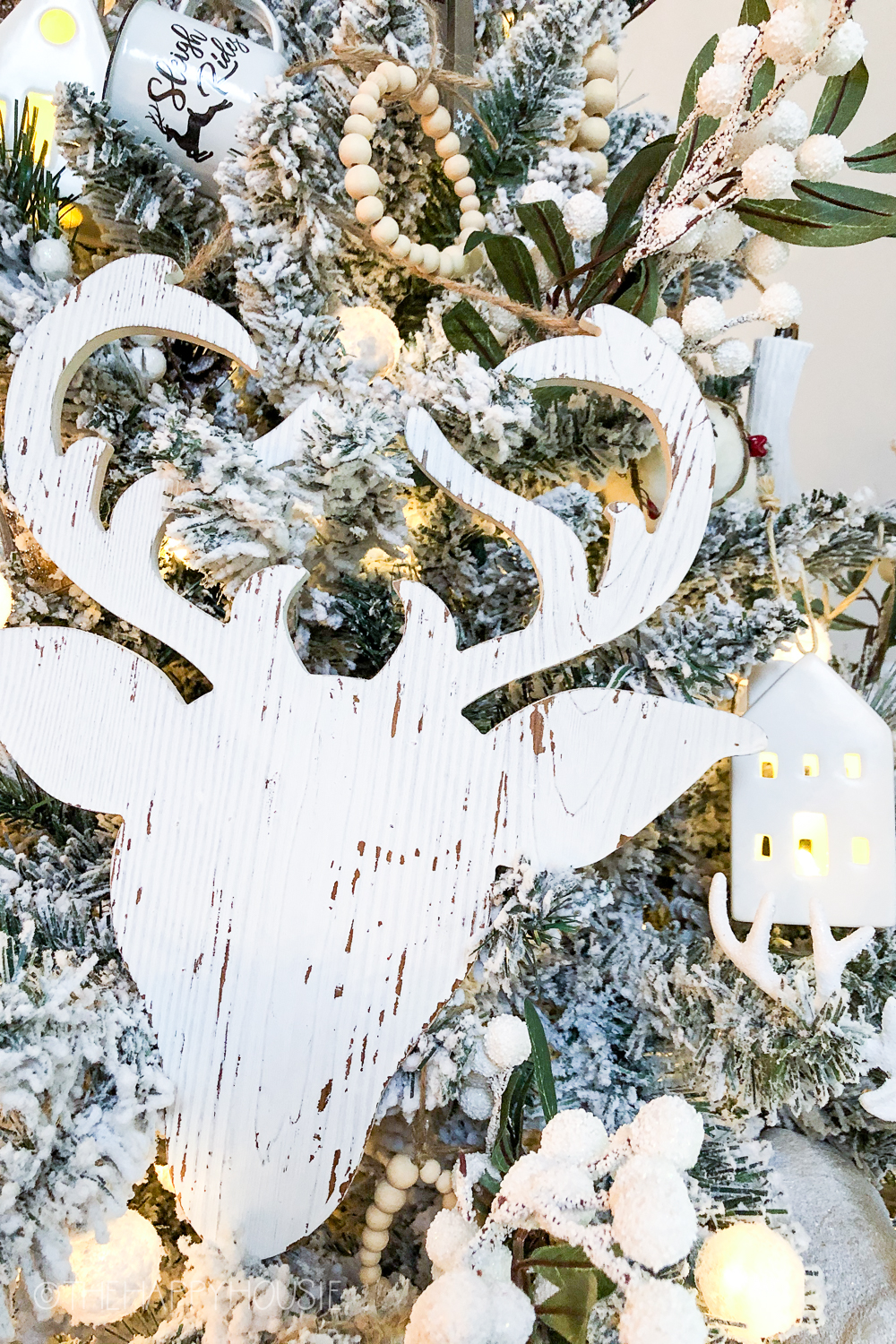 A wooden deer with antlers painted rustic white on the tree.