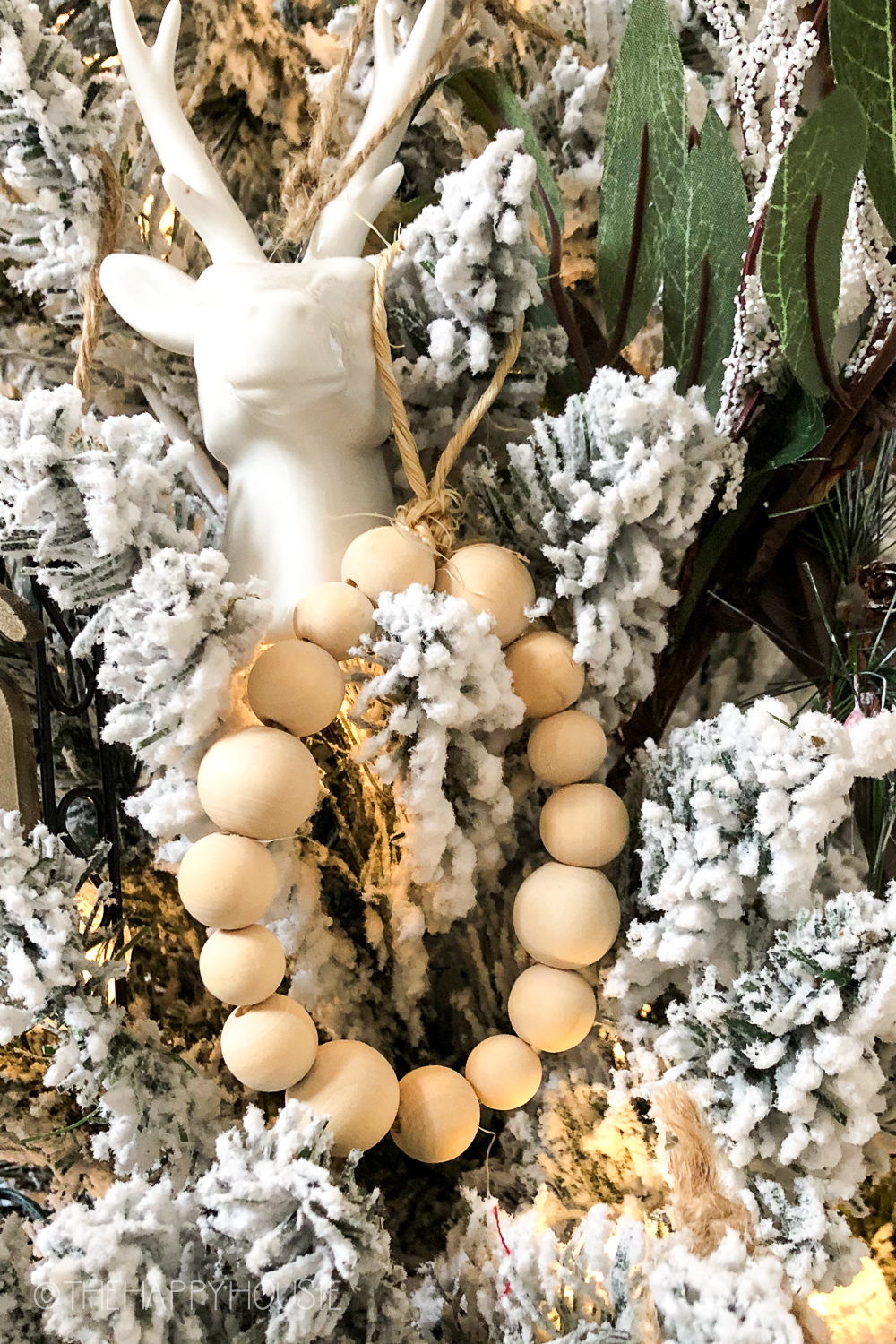 A flocked Christmas tree with a deer ornament and wooden beads.
