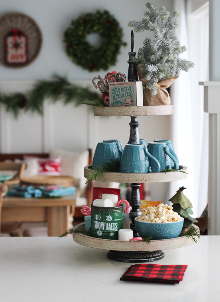A 3 tiered tray on the kitchen counter with mugs and popcorn on it.