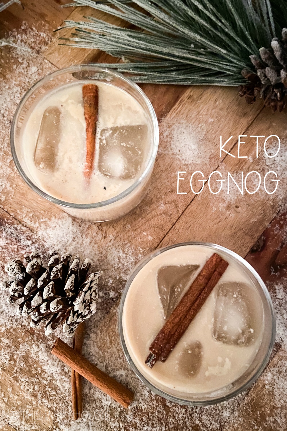The eggnog on the snowy table beside a pinecone an evergreen with sticks of cinnamon.