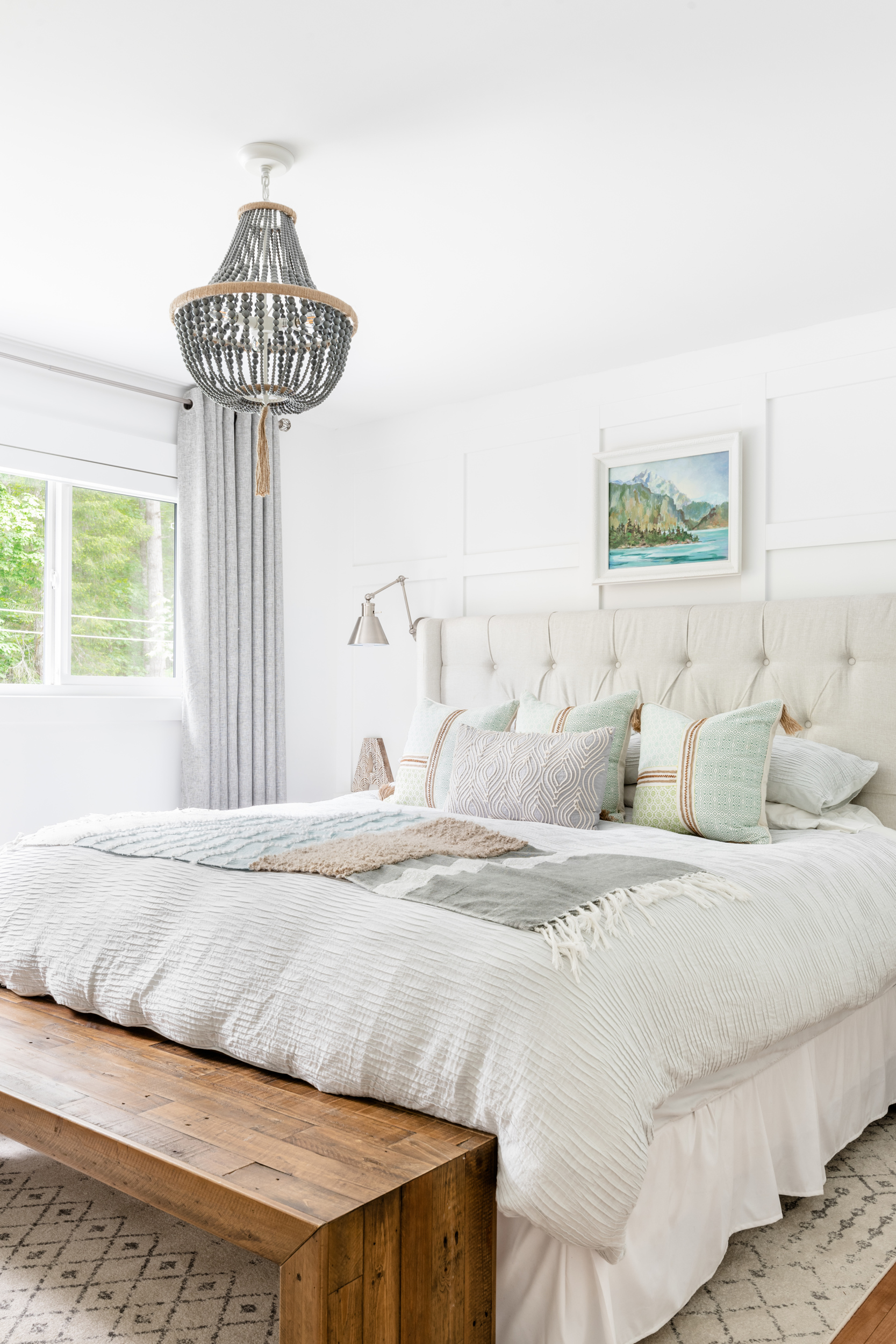 an updated bedroom with a tufted upholstered bed and wood bench and beaded chandelier
