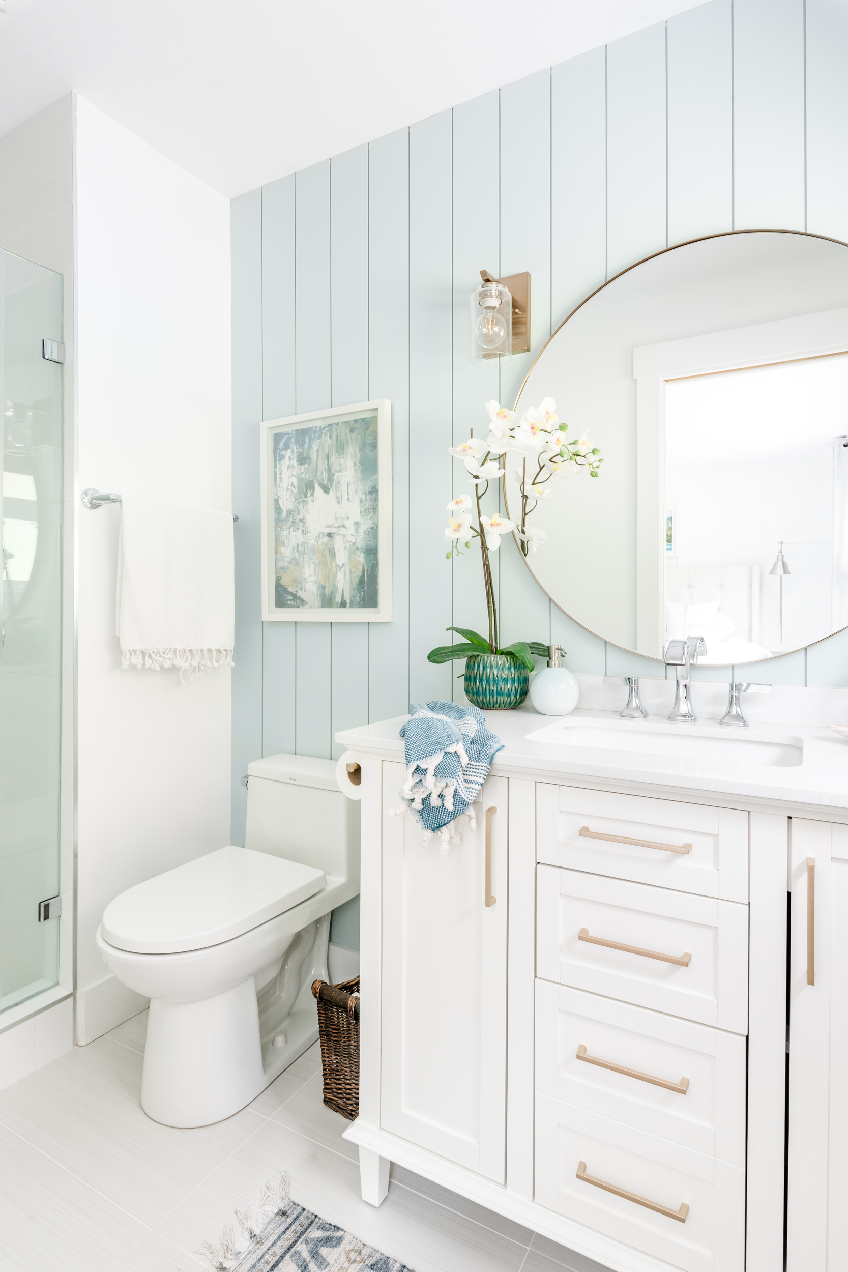 a light bright newly renovated bathroom with gold hardware, lighting, and mirrors and a blue vertical shiplap feature wall