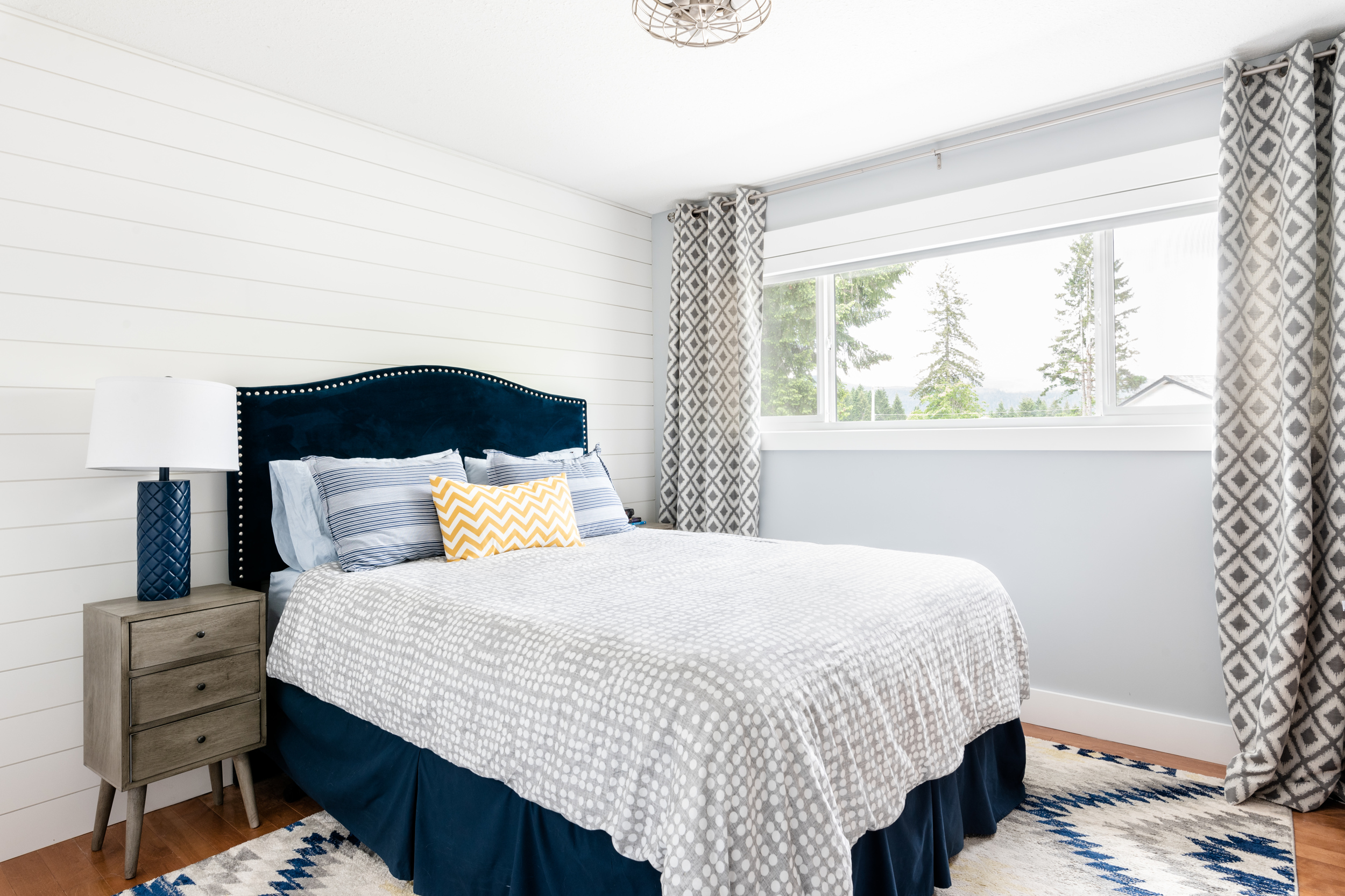 a boys bedroom with a white shiplap feature wall and blue velvet nailhead headboard 