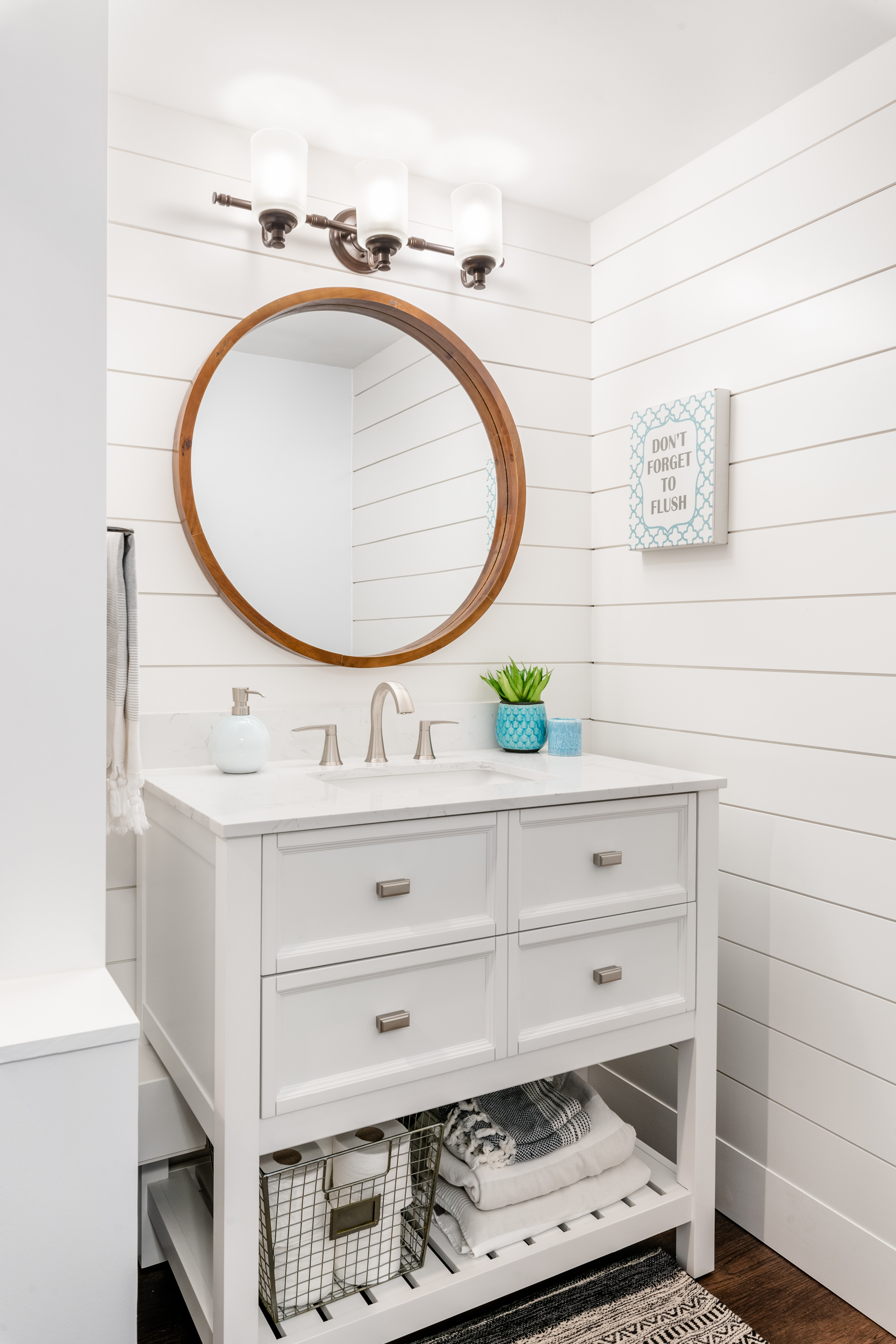 shiplap feature walls around a white vanity with a round wooden mirror