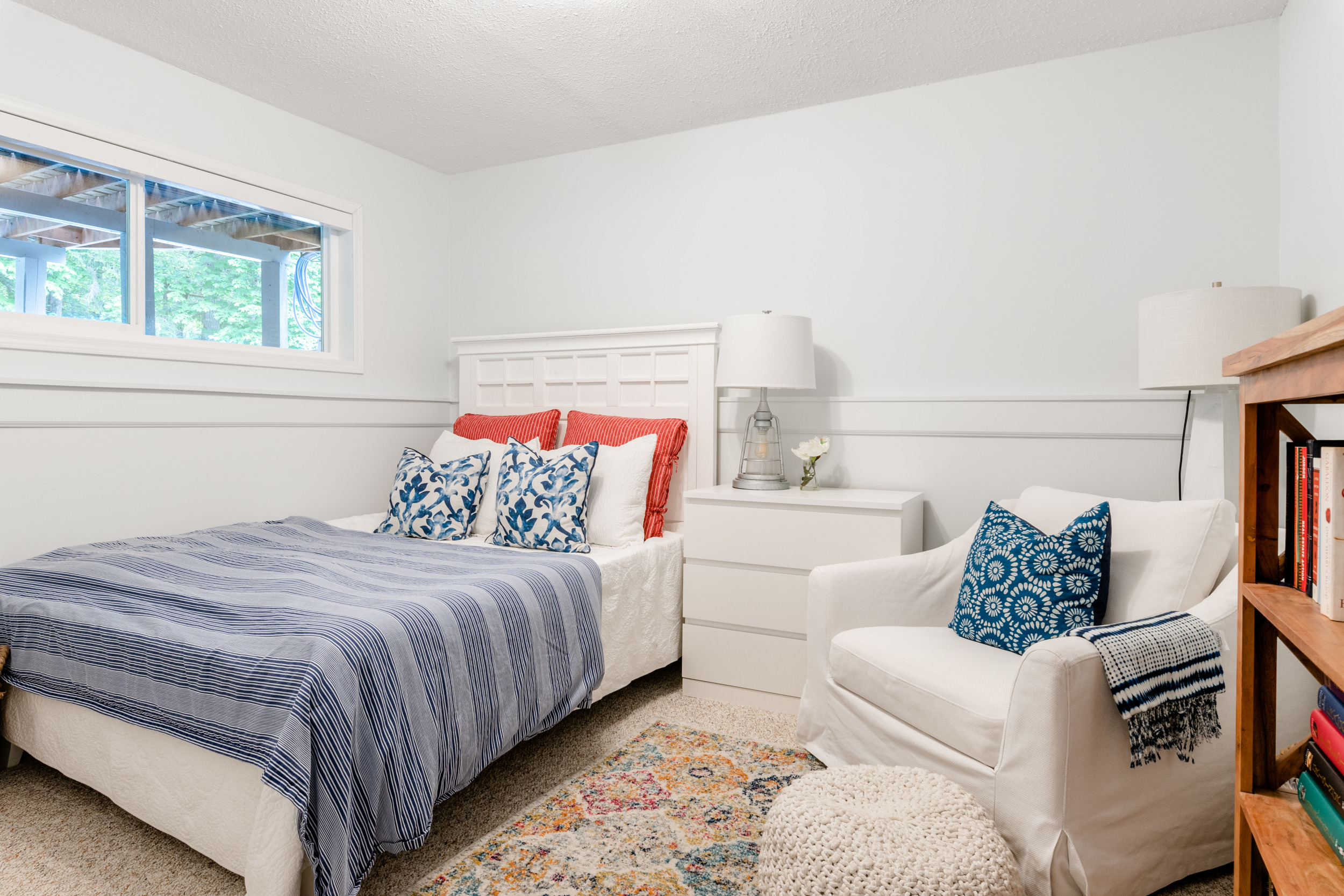 a light and fresh newly painted basement guest bedroom with a panelled bed and white cozy chair