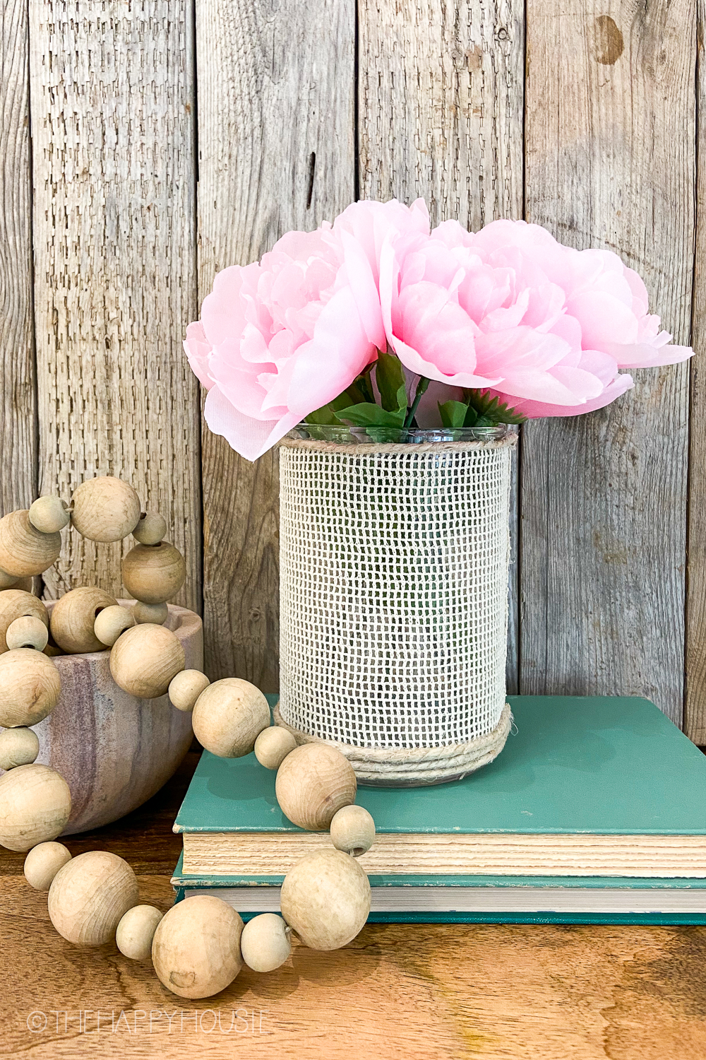 There are wooden beads beside the peonies in a vase.