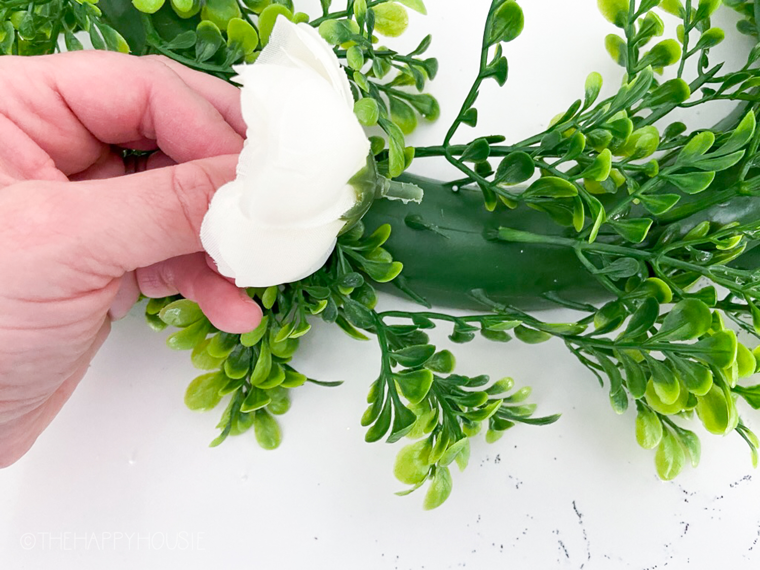 A faux white flower attaching it to the green wreath.