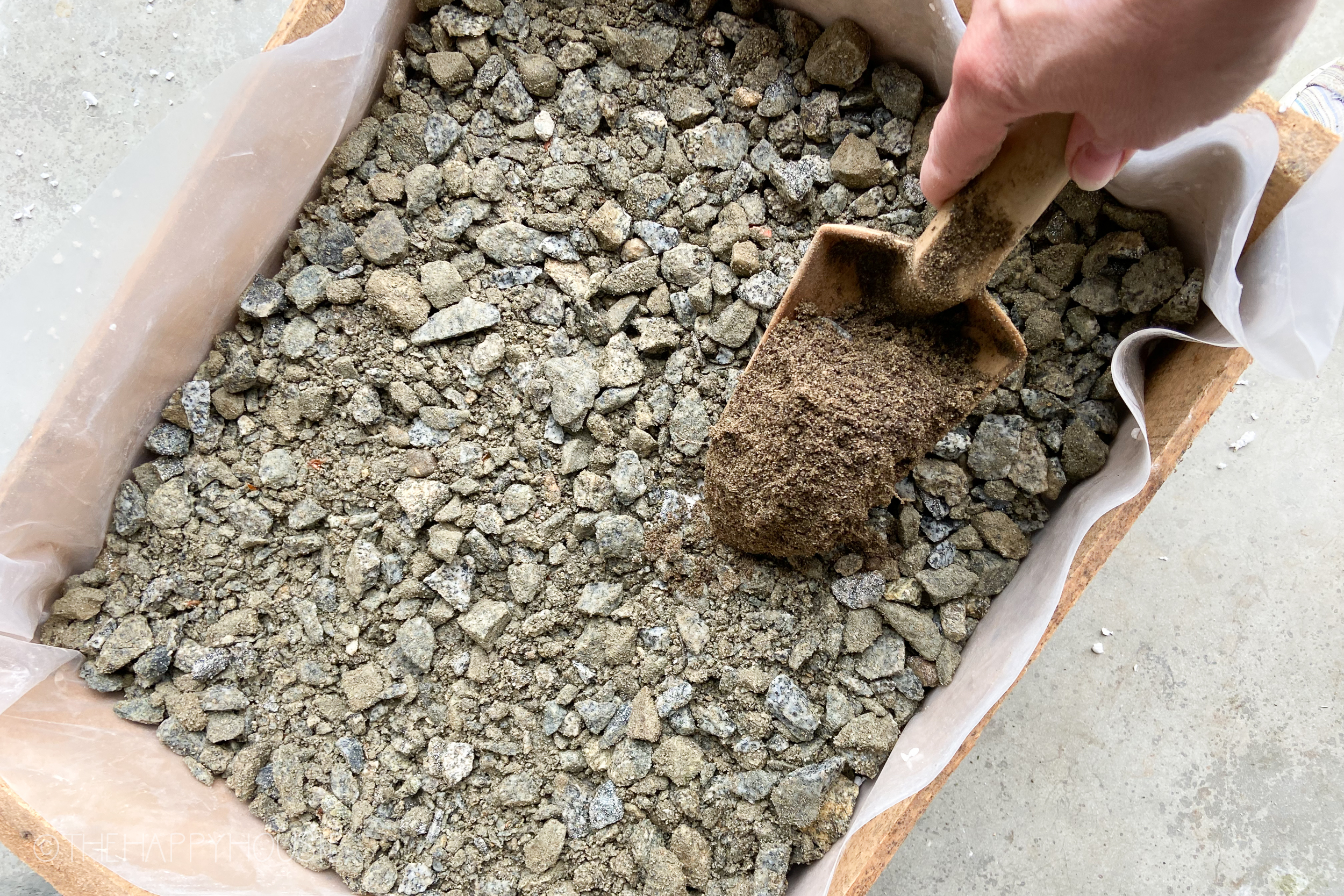 Scooping soil on top of the rocks in the wooden box.