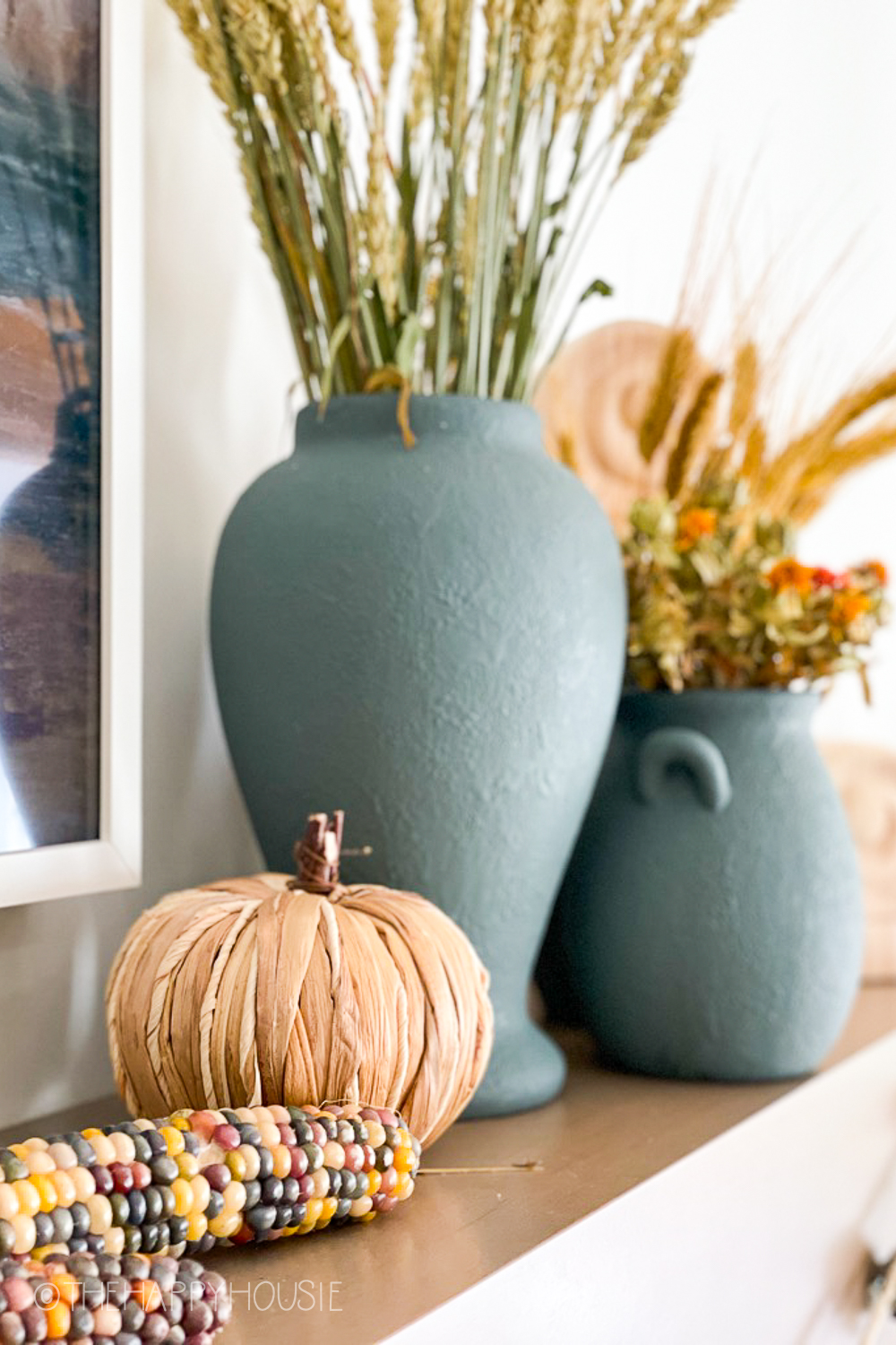 A corn husk pumpkin is beside the vases on the mantel.