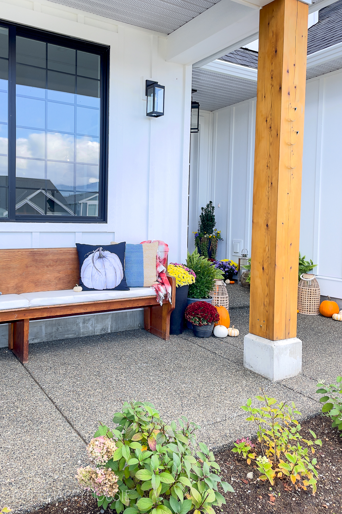 On the front porch there is a small wooden bench with throw pillows on it.