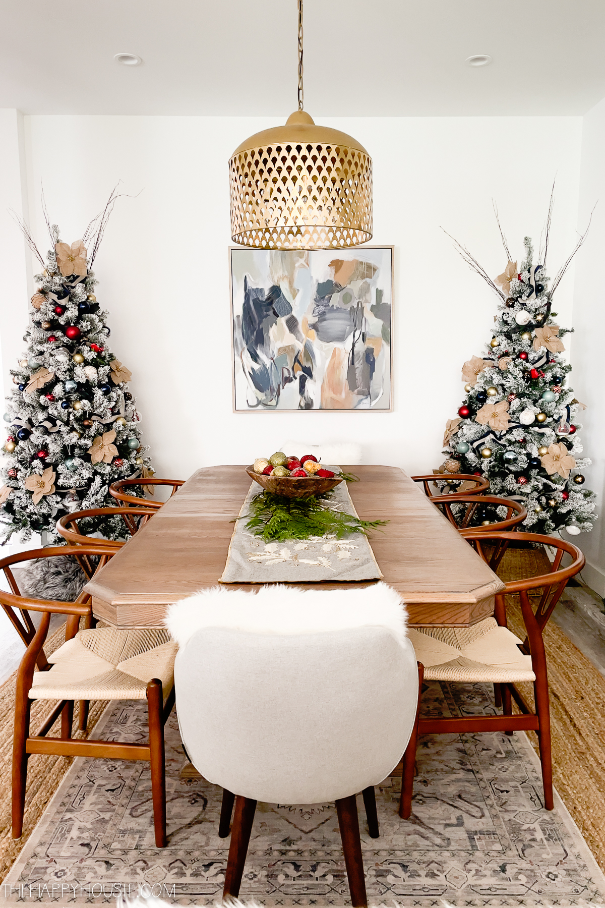 A dining room table with two Christmas trees in the corner.
