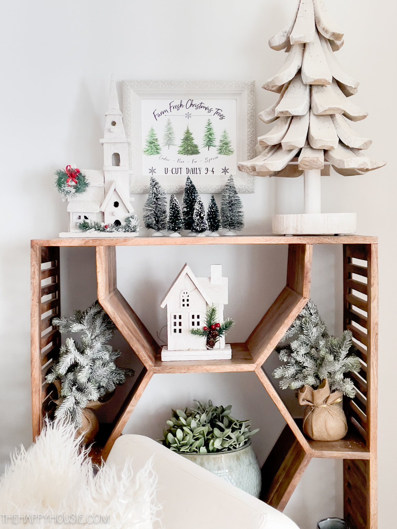 There is a small wooden Christmas house and a wooden Christmas tree on the shelf.
