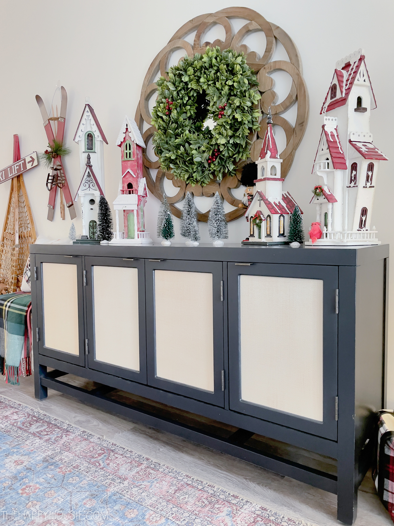 A side console table with Christmas houses on it and a wreath above it.