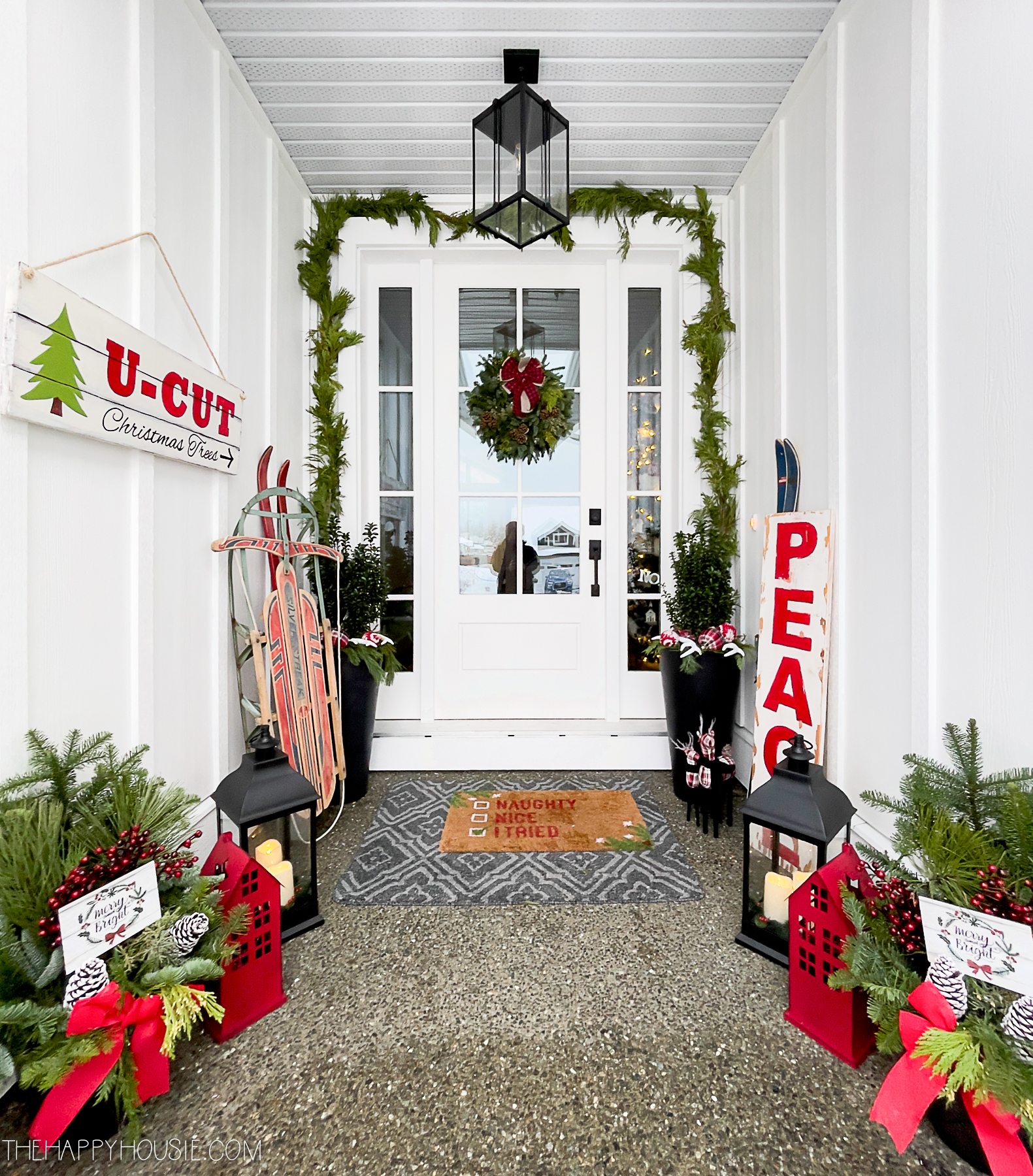 a modern farmhouse front porch decorated with red, white, and black Christmas decor