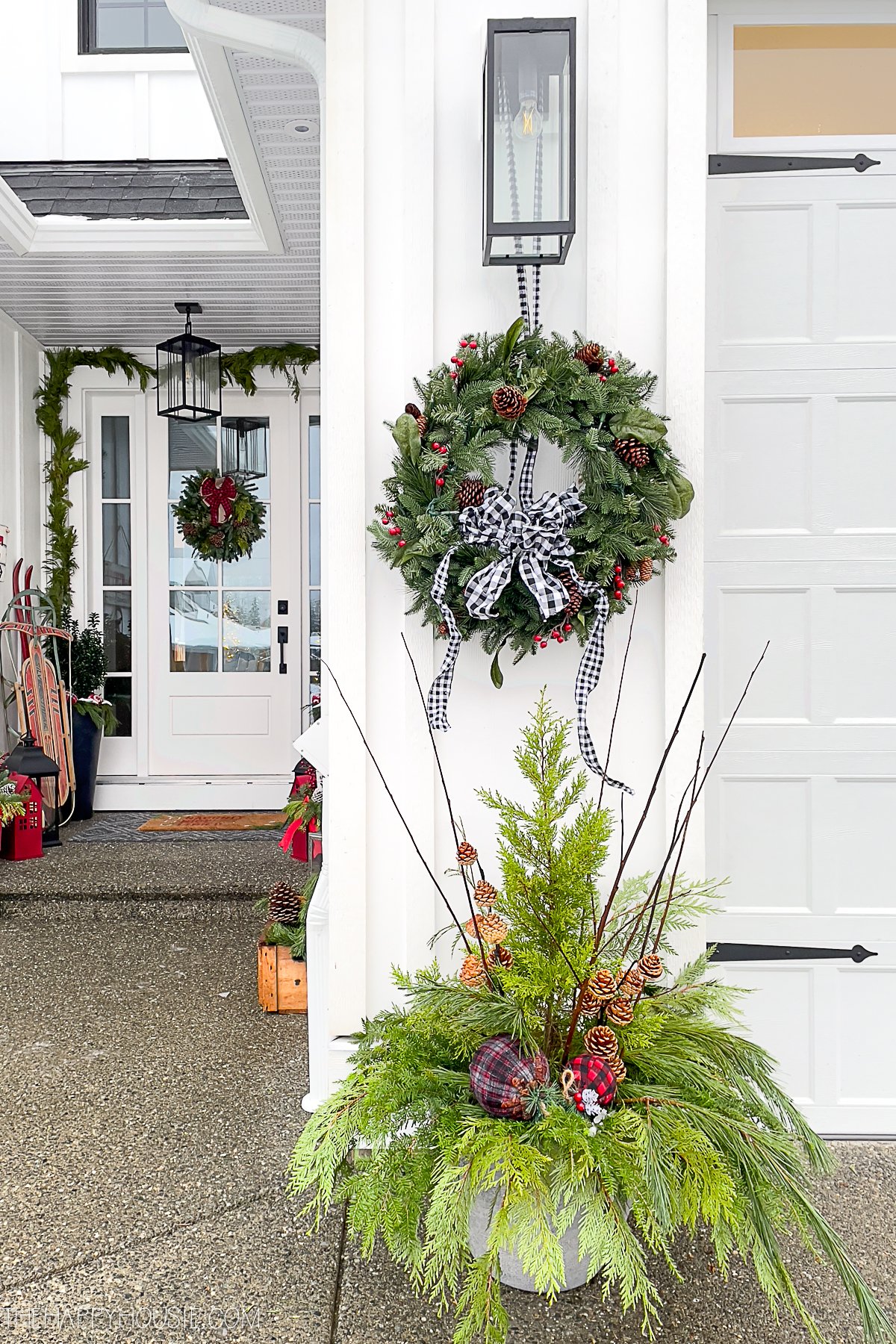 a wreath and pot full of greenery displayed at the front of a garage.