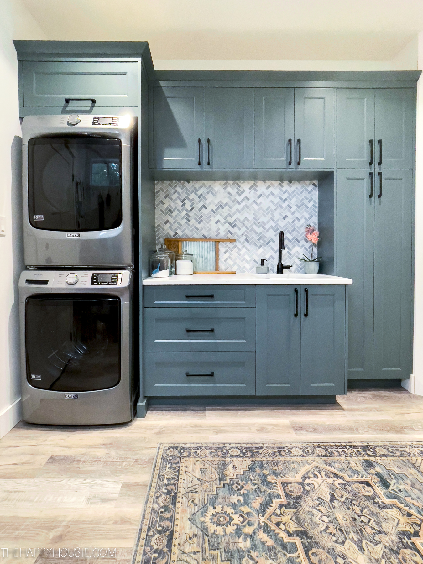A laundry room with blue/grey cupboards and a modern washer and dryer.