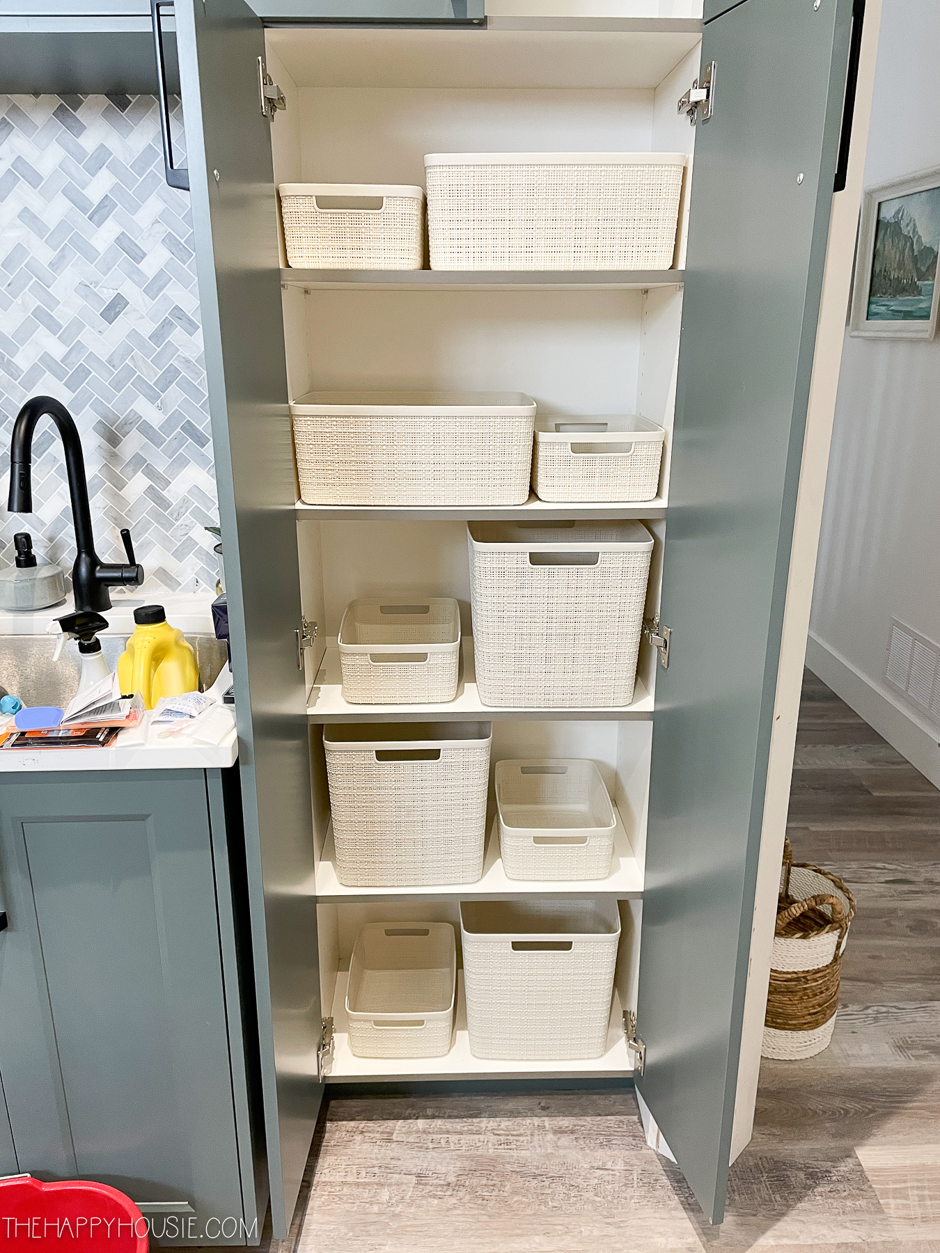 The open cupboard doors beside the sink with white basket only on the shelves.