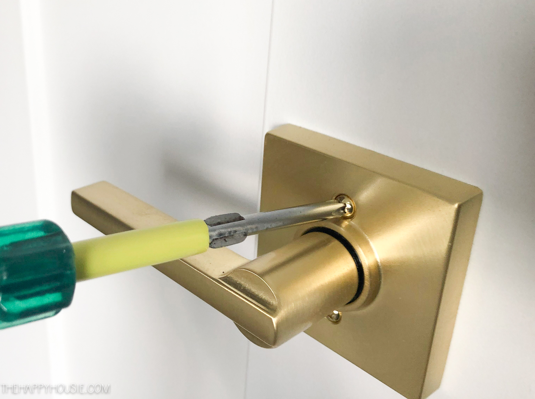 a screwdriver tightening on a new interior door lever set by Schlage in a satin brass finish
