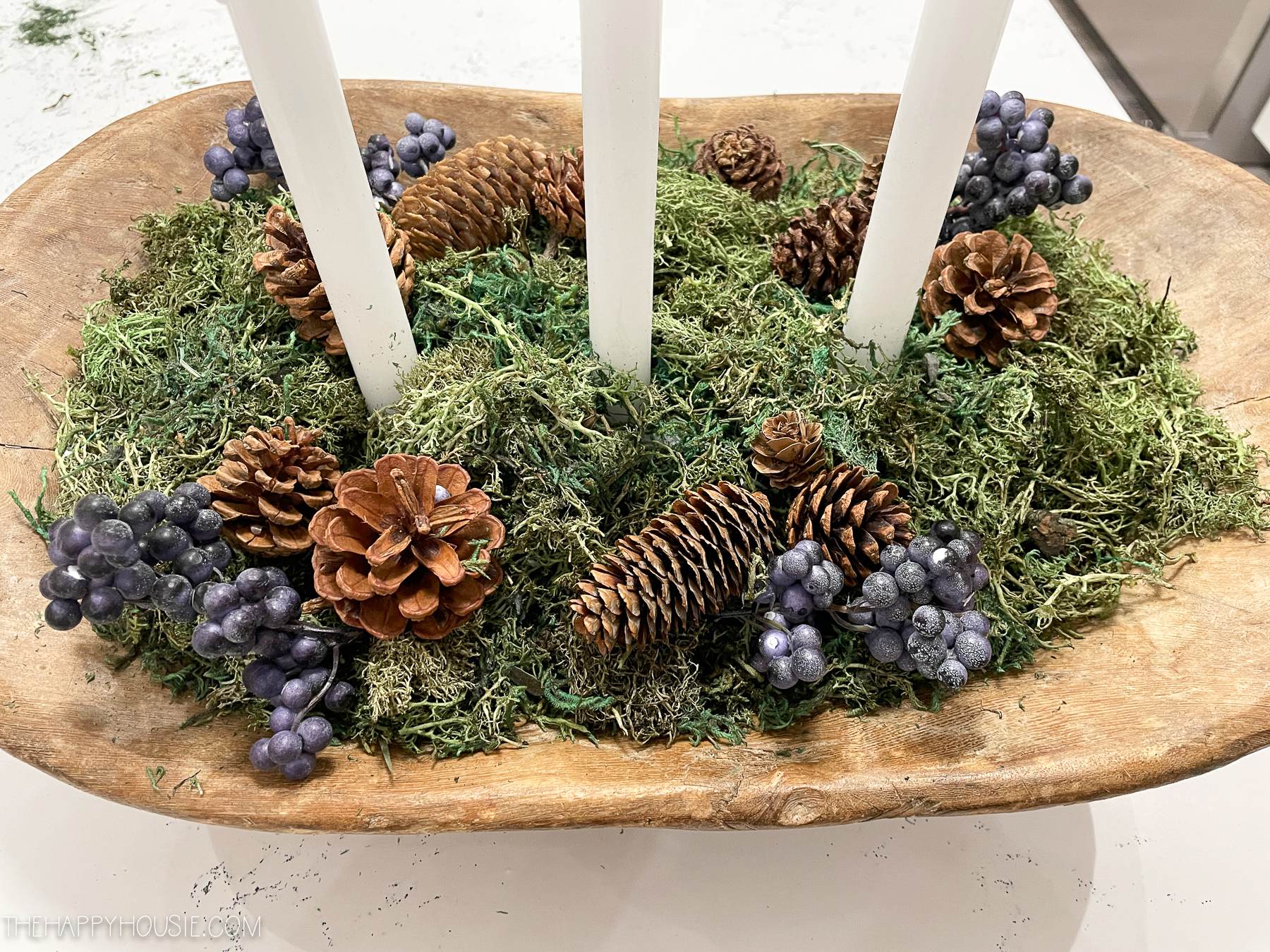 A dough bowl with pine cones, purple berries and candles.