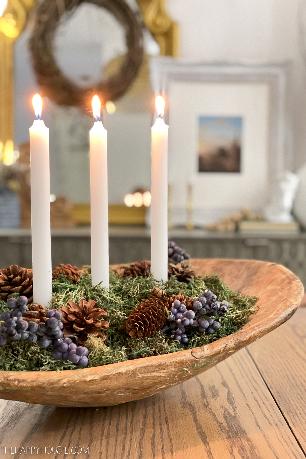 A dough bowl with moss, pine cones and candles in it.