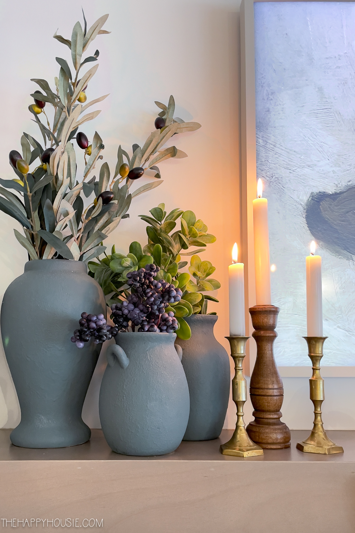 Candles on the mantel beside olive branches.