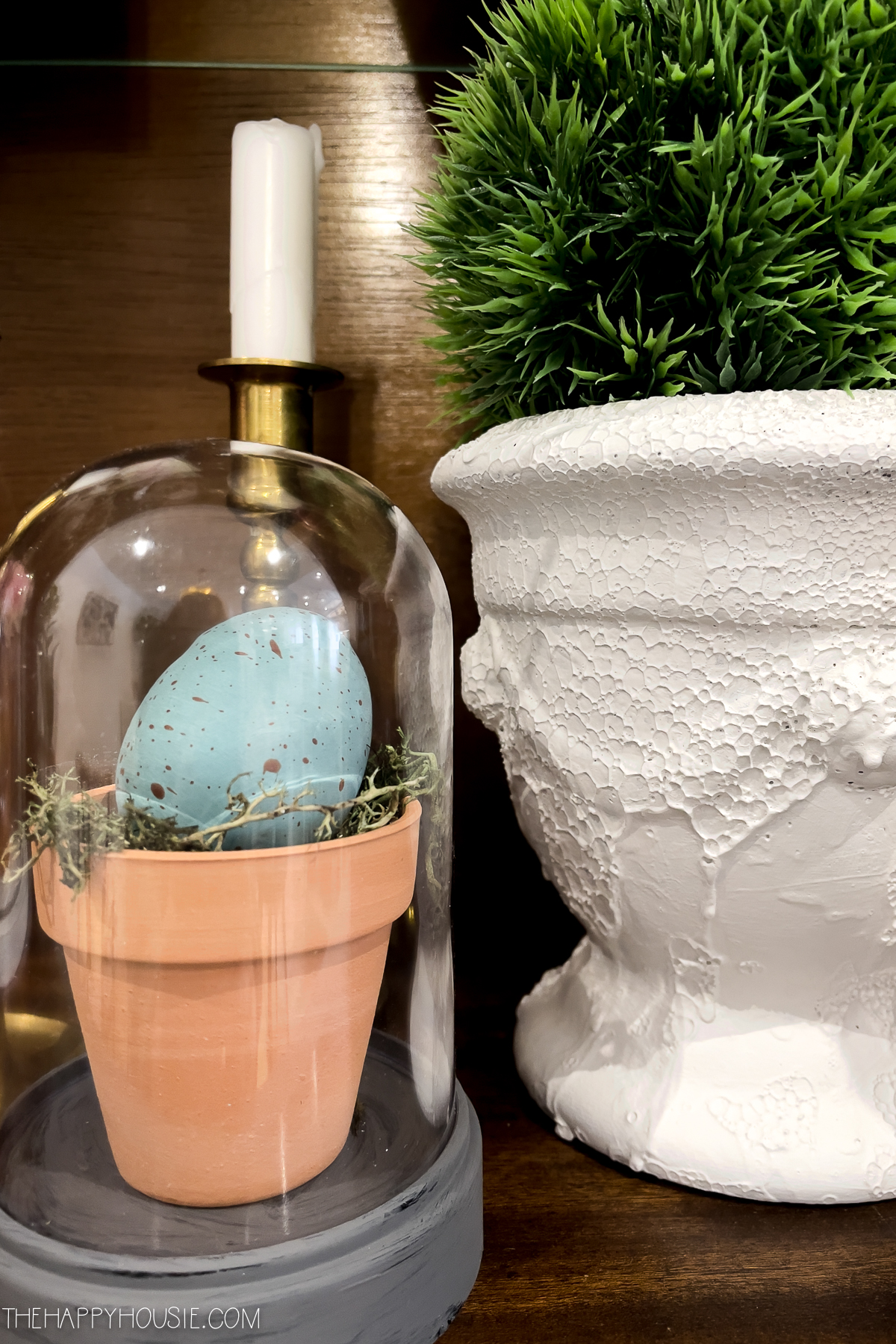 a miniature cloche with a decorated faux Easter egg sitting in a tiny pot on a bed of moss