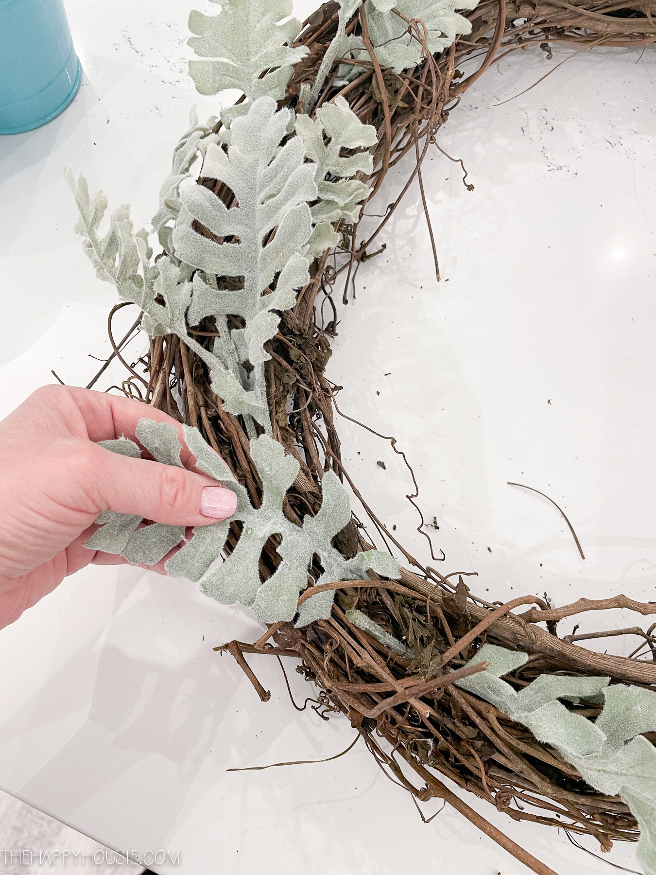inserting faux greenery branches into a grapevine wreath form