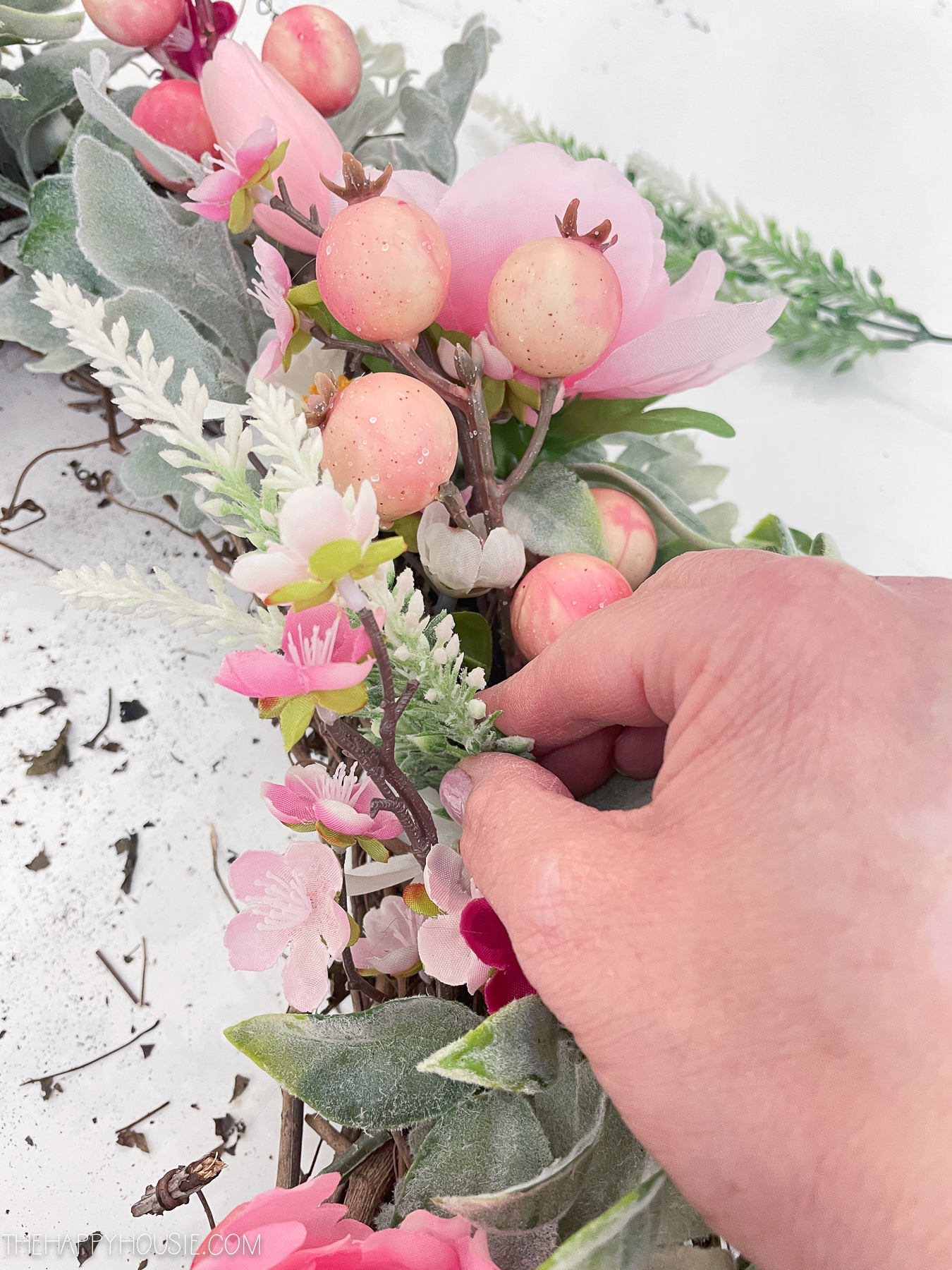 using hot glue to attach faux floral branches into a grapevine wreath form