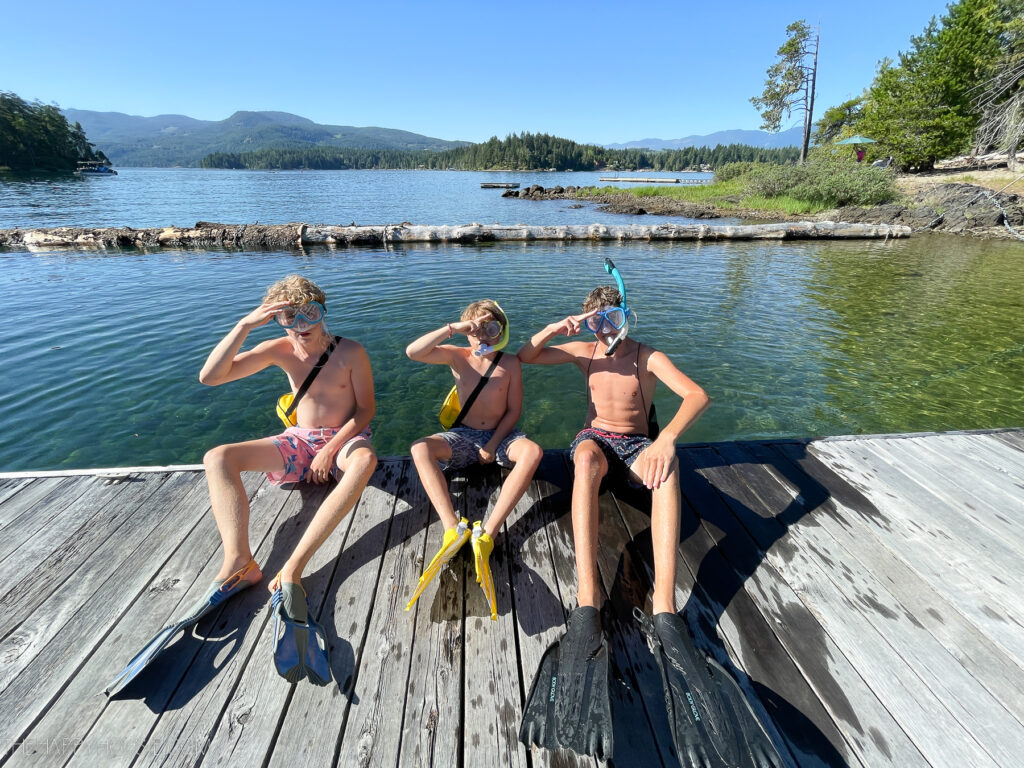 three boys on a dock on a lake with snorkel gear 